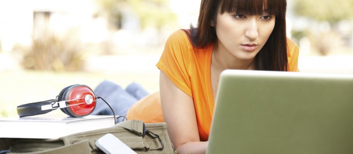 Girl using laptop on grass, headphones, satchel